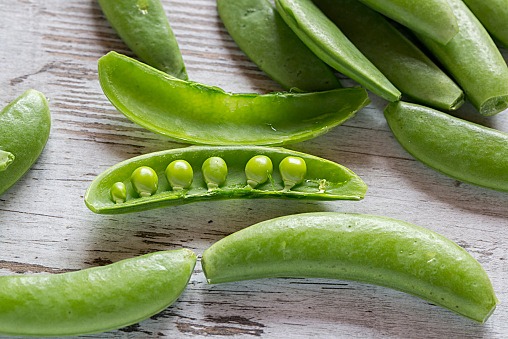 Whole and opened peasecods of snow peas on wood