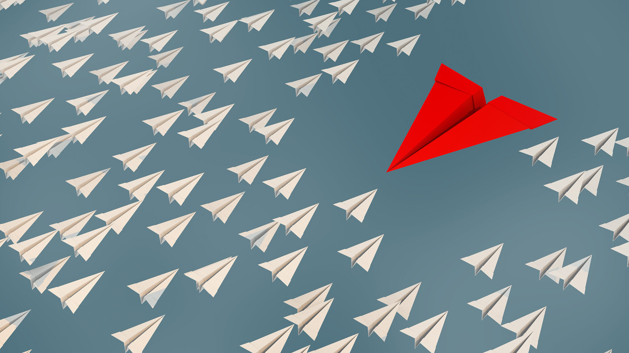 one large red paper airplane flying in the opposite direction of many other small white paper airplanes